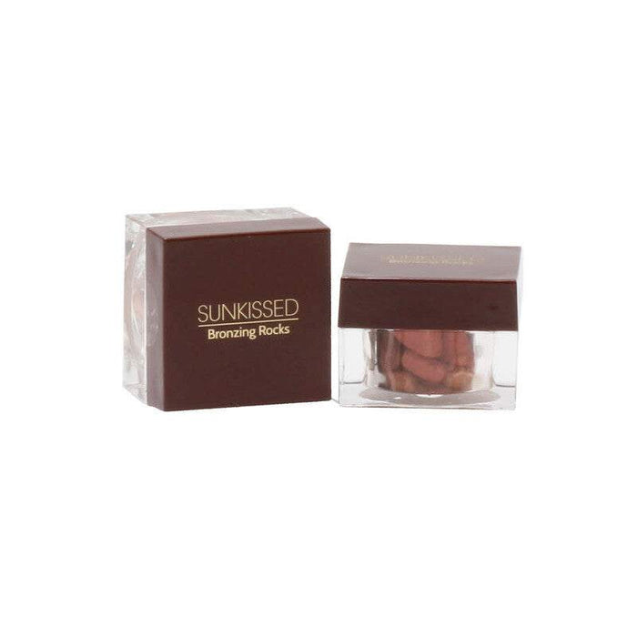 Sunkissed Bronzing Rocks bronzer in a clear jar with brown pressed powder pieces and a dark brown rectangular box