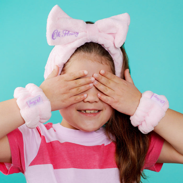 Child wearing a Oh Flossy pink headband with bow and matching wrist against a teal background